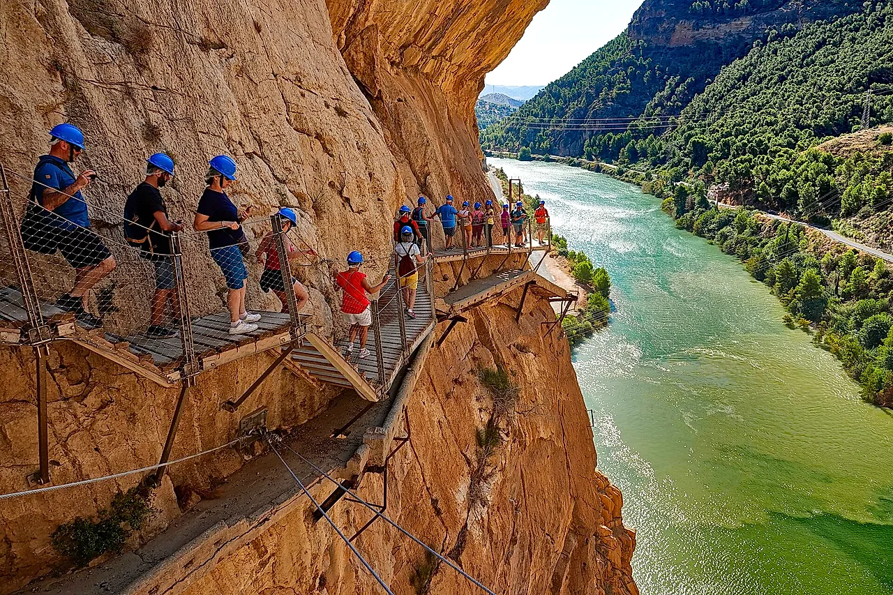 Escursionisti con il casco sulla passerella del Caminito del Rey sopra il verde fiume Guadalhorce
