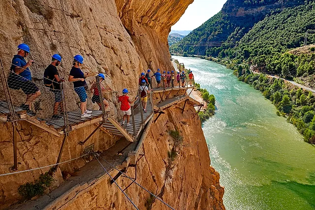 Escursionisti con il casco sulla passerella del Caminito del Rey sopra il verde fiume Guadalhorce